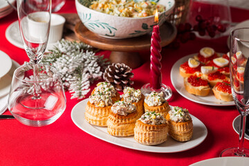 Served Christmas table with homemade food, different appetizers, vol-au-vent  with chicken salad, canape with caviar and egg, bottle of wine, candles and decoration. Life style foto of dinner party.