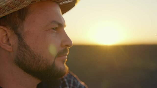Tired farm worker relaxing after hard working day in farmland, side portrait. Inspired farmer thinking about future harvest and profit, agribusiness and farming, face of bearded man in straw hat