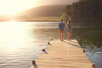 Back, couple and holding hands at lake for love, sightseeing and travel for anniversary. Summer vacation, man and woman on pier with romantic gesture, relationship development or commitment in nature