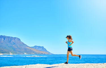 Fitness, running and girl on beach with blue sky, marathon training or outdoor exercise on mockup space. Ocean, mountain or woman runner on morning workout in nature for body care, health or wellness