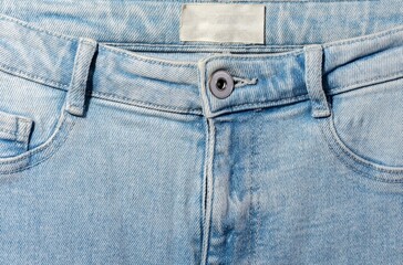 Blue jeans front view with blank white label, metal button and close up denim texture.