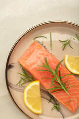 Red fish. Raw salmon fillet with rosemary and lemon on light background. Vertical photo