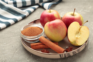 Red apple, cinnamon sticks and cinnamon in bowl on grey concrete background.
