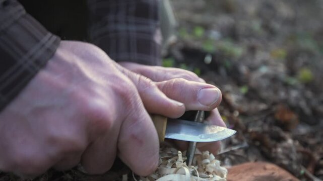 A man ignites fire using a knife and firestarter, creating sparks over wood shavings. This close-up captures the essence of survival skills and outdoor bushcraft