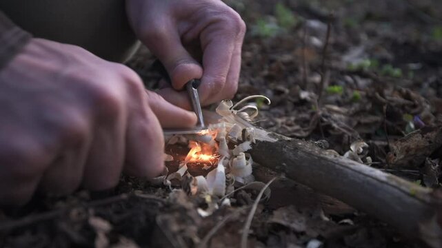 A man ignites fire using a knife and firestarter, creating sparks over wood shavings. This close-up captures the essence of survival skills and outdoor bushcraft
