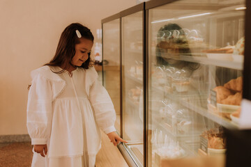 A little girl looks at a dessert display case in a cafe