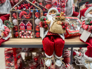A traditional figure of Santa Claus in a red suit sits in a store against the background of other bright and shiny New Year's toys. Holiday home decor. Traditional christmas decoration.