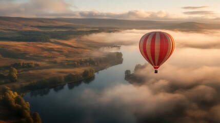 Obraz premium A vibrant hot air balloon floats above a misty river, surrounded by rolling hills and lush landscapes bathed in soft morning light