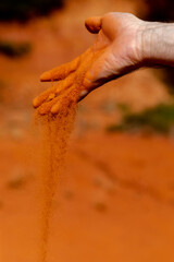 Red ochre sand runs through hand with red sand rocks as background
