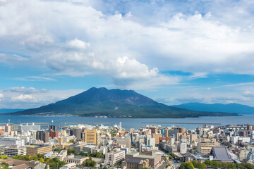 Obraz premium Cityscape with Sakurajima mountain, sea and blue sky background view from Shiroyama Park Observation park, Kagoshima, Kyushu, Japan