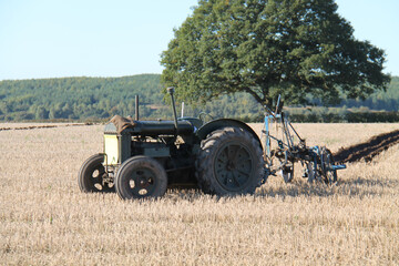 A Farming Tractor and Vintage Plough Cutting Fuurrows.