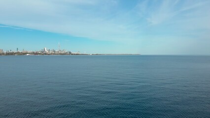 Toronto skyline rises peacefully over calm waters of Lake Ontario, blending modern architecture with serene natural beauty. Expansive lake and blue sky, harmony between city and nature in Canada