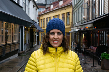A young brunette woman, around 30 years old, wearing a yellow puffer jacket and a blue knit hat,...