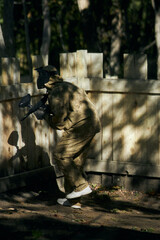 Paintball player in protective mask aims gun, takes cover under fire, paint splashes. Paintball player hide behind wooden barricade, shooting paintballs. Paintball players.