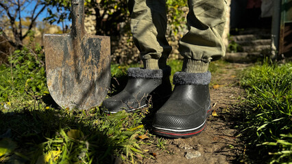 Gardener in sturdy footwear standing on a garden path with a shovel during a sunny autumn day
