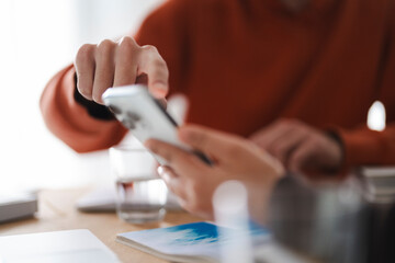 A man in an orange hoodie points at a smartphone held by a woman, engaging in a collaborative learning activity, with a friendly interaction.