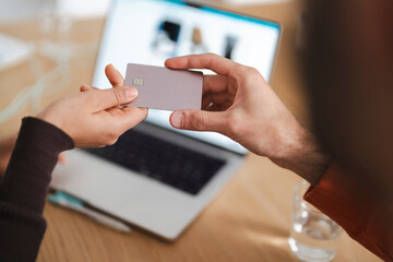 A woman holds a credit card near a laptop displaying online shopping options while collaborating with another person, illustrating a casual online shopping experience and teamwork.