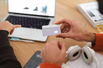 A man holds a credit card as he and a woman browse an online shopping website on a laptop, creating a scene that represents e-commerce, teamwork, and shared decision-making in a cozy workspace.