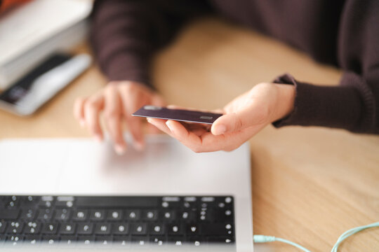 A woman holds a credit card in her hand while browsing an online shopping site on her laptop, portraying an engaging scene of digital purchasing in a relaxed home workspace.
