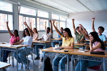 Happy group of multi-ethnic students sitting in classroom with their hands raised. Young smiling multiracial teenagers people answering the teacher question in class. Generation z high school concept