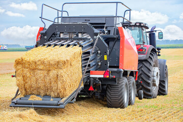 Obraz premium Baling hay during a sunny afternoon on a vast farmland with vibrant blue sky