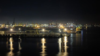 night scene shot commercial port loading and unloading cargo from container ship import and export by crane for distributing goods by trailers transported to customers and dealers,