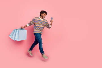 Full size photo of nice young man jump run phone bags wear pullover isolated on pink color background