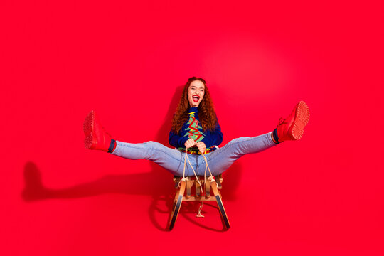 Full size photo of pretty young girl ride sledge spread legs wear blue christmas outfit masquerade theme party on red color background