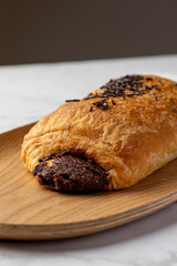 A delicious chocolate croissant sits on a wooden plate, topped with chocolate sprinkles, capturing the essence of a perfect bakery treat with a rustic touch.