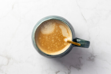 This image shows a top-down view of a frothy coffee in a textured turquoise mug, set against a softly veined marble background, creating a cozy aesthetic appeal.