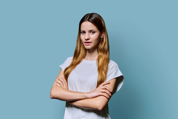 Fototapeta premium Beautiful young girl with crossed arms looking at camera on blue background