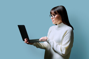 Serious middle aged woman using laptop on blue background