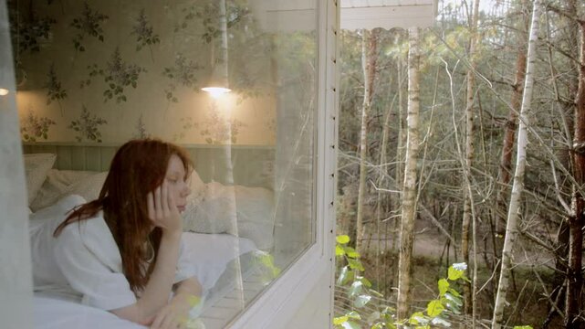 young woman looking outside apartment. Attractive lady watching beautiful forest view 