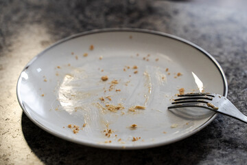 Dirty white ceramic plate with leftovers of food and fork, top view