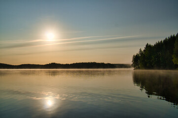 Lake in Sweden at sunrise with romantic light, blue water and trees on the shore