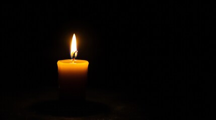 One lit candle burns brightly on a black background