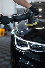 Professional man with polishing tool polishing black car in garage . Detailing. Varnish care and...