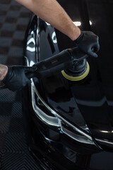 Professional man with polishing tool polishing black car in garage . Detailing. Varnish care and...