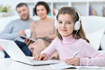 Cheerful little girl using a laptop at home with her parents in the background.