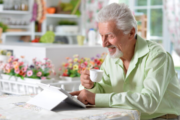 Elderly man posing at a table with a tablet