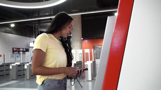 Young woman is buying a train ticket at a self-service terminal