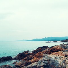 Tranquil seascape with rocky shore and distant mountains.