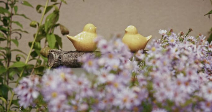Yellow ceramic birds on a log amid purple flowers in Kumrovec, Croatia's rustic charm