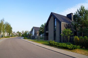 Street with Barn House along asphalt road in gated community. Modern house in suburb. Wooden Scandi...