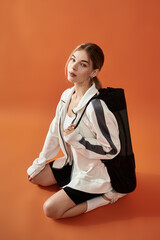 The sportswoman sits gracefully against a vibrant orange background, radiating confidence.