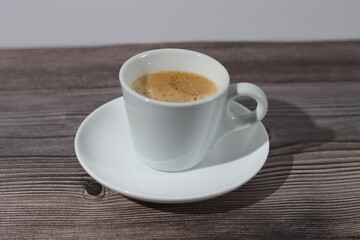 A white cup of espresso with its saucer on a wooden pattern with a white background.