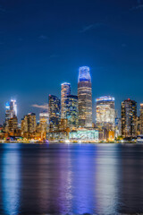 Naklejka premium A vibrant city skyline at night with towering skyscrapers and bright lights reflecting on the water, showcasing the beauty of urban architecture. Generative AI