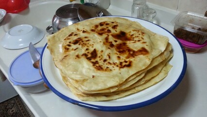 A plate of freshly made flatbreads, their golden-brown spots reflecting the warmth and tradition of homemade food, symbolizing the comfort and simplicity of traditional cuisine shared among family.