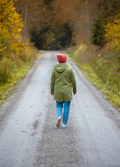 middle-aged caucasian woman in hat and jacket is walking by trail in the autumn forest 