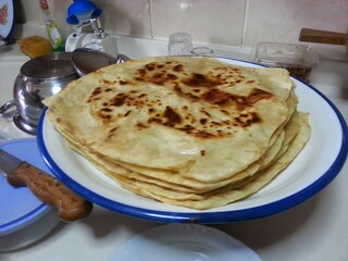 A plate of freshly made flatbreads, their golden-brown spots reflecting the warmth and tradition of homemade food, symbolizing the comfort and simplicity of traditional cuisine shared among family.